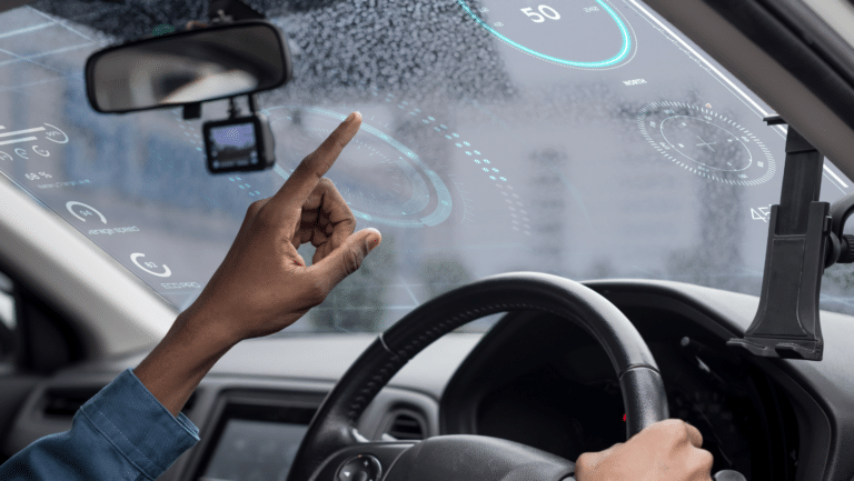 A person inside a car interacts with a futuristic augmented reality dashboard projected onto the windshield, featuring various digital gauges and information. The driver monitoring system enhances safety as the drivers hand reaches towards the virtual interface.